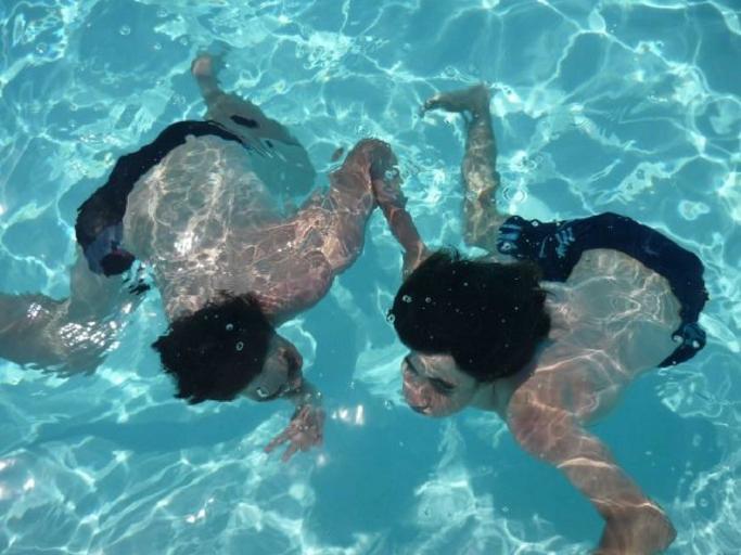 Dvaja ľudia v plavkách sa ponárajú v bazéne.jpg