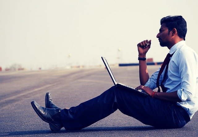 Muž v košeli sedí na ceste s notebookom a premýšľa